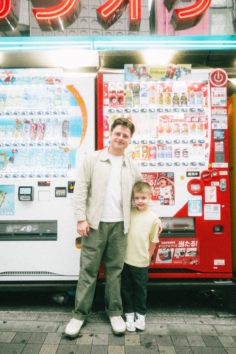 Andy Sommer and his son in front of a bank of lit Tokyo vending machines at night