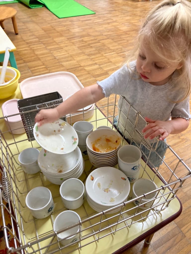 Andy Sommer's two year old daughter reaching up to stack her used bowls and cup into the dish rack at preschool