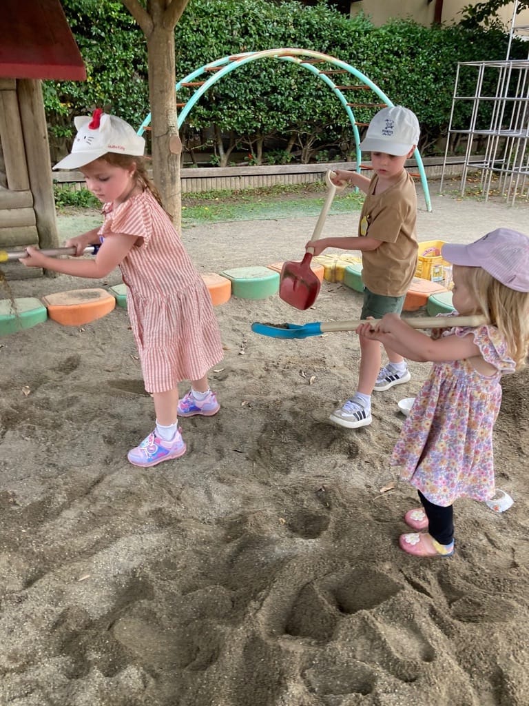 Children in matching sun hats digging in the preschool sandpit