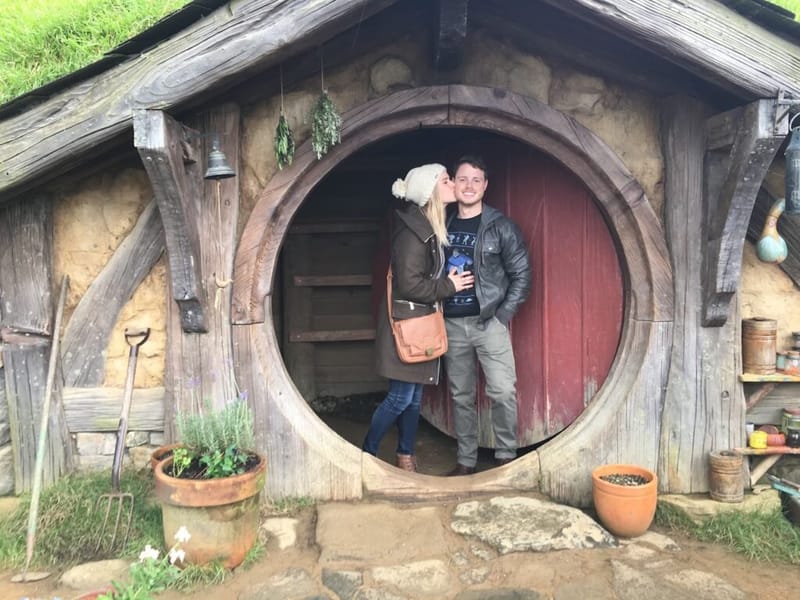 A parent and child in the round doorway of a Hobbit hole at Hobbiton.