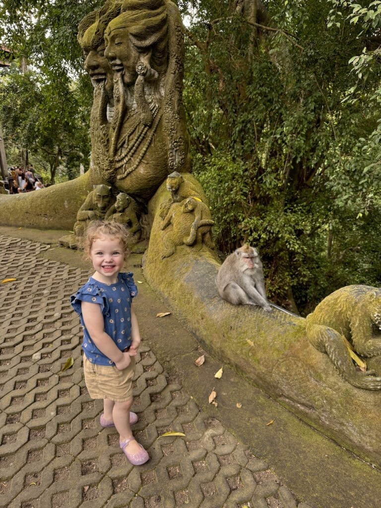 A young boy on a stone path beside a carved statue in Bali.