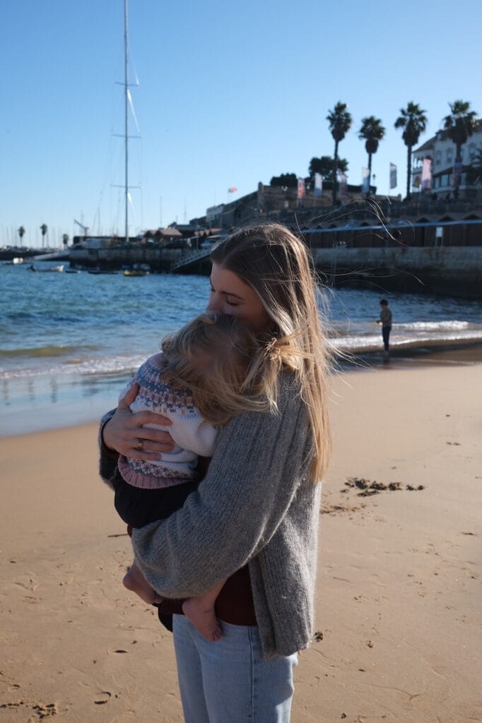 A parent holding a child on a windy coastline.