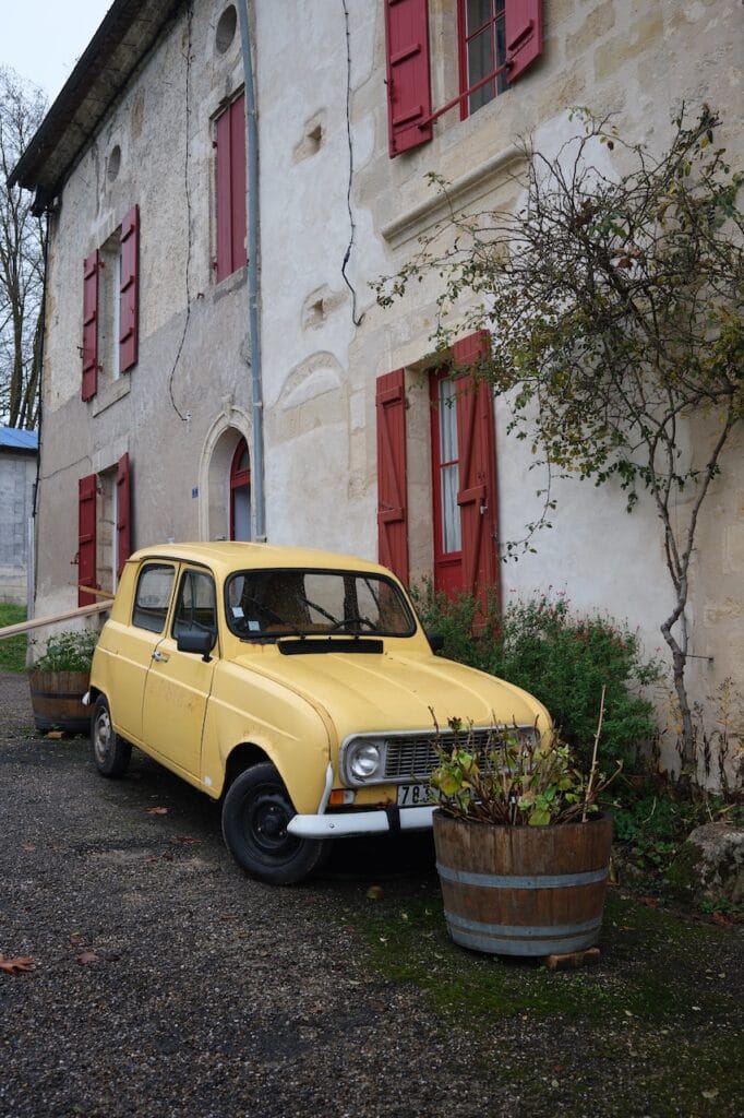 A vintage yellow car parked beside a stone building in France.