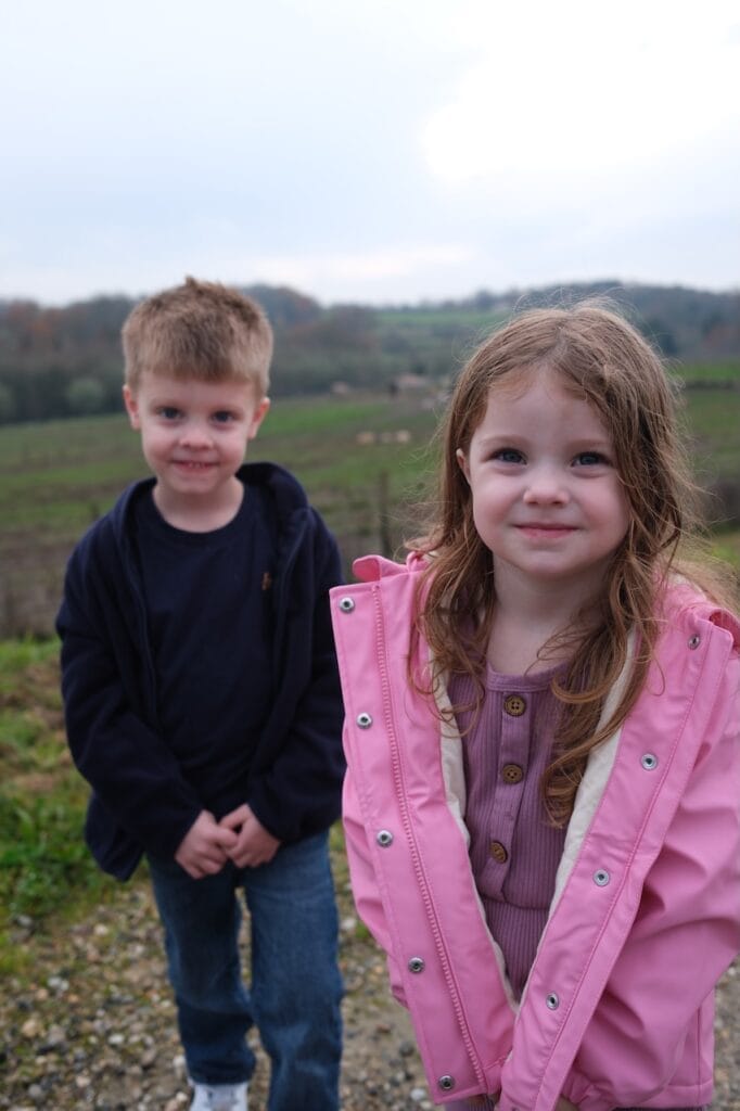 Two of the children smiling outdoors, one in a pink coat.