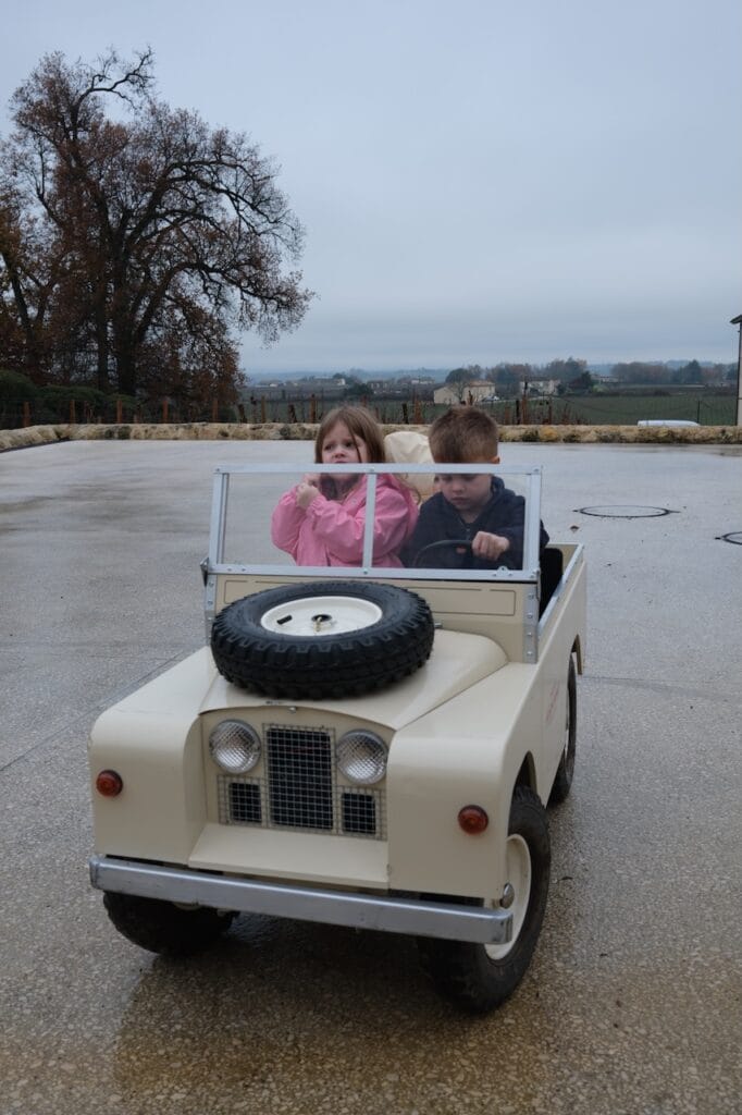 A Sommer child driving a toy electric jeep near the water.