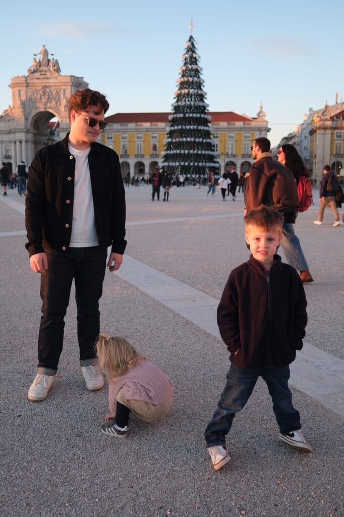 The family walking near a tall Christmas tree in a Lisbon square at dusk.