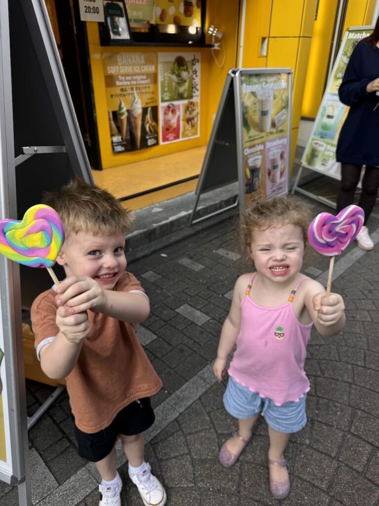 Two young children holding colorful lollipops on a city street.