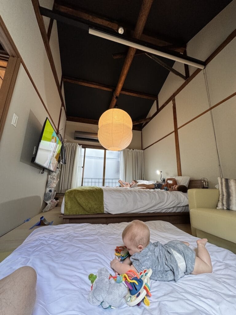 A child resting on a bed in a rustic room with a paper lantern.